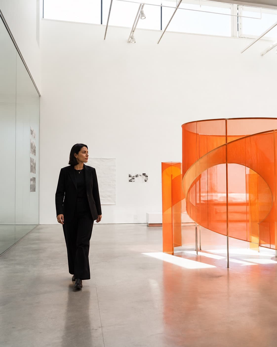 Directora creativa caminando hacia una instalación translúcida naranja dentro de un estudio contemporáneo.