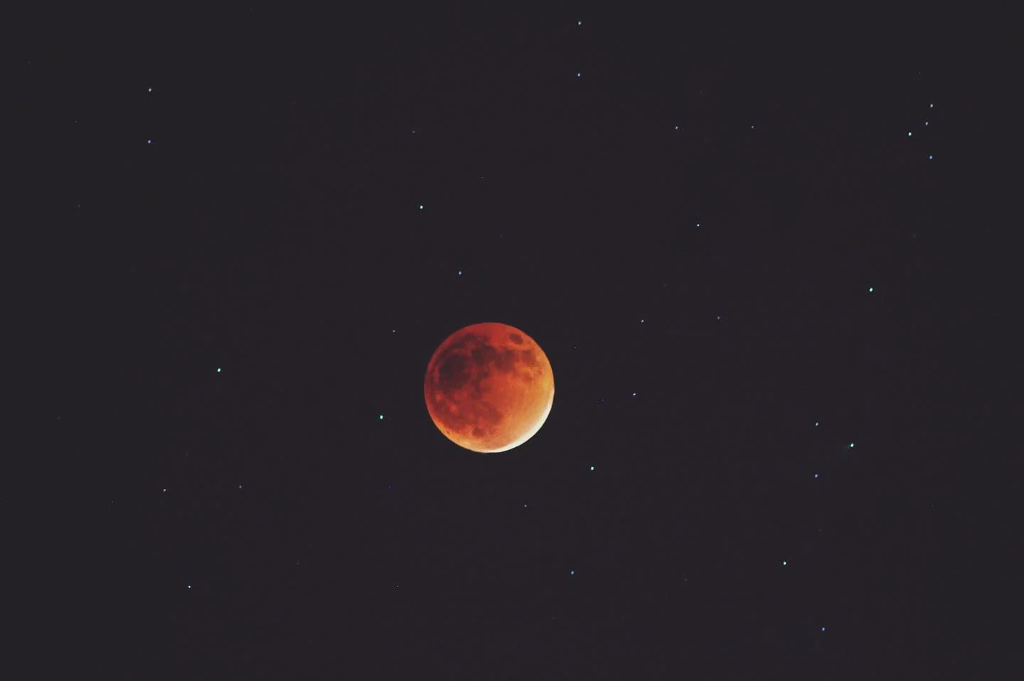 A red lunar eclipse surrounded by stars in a dark sky