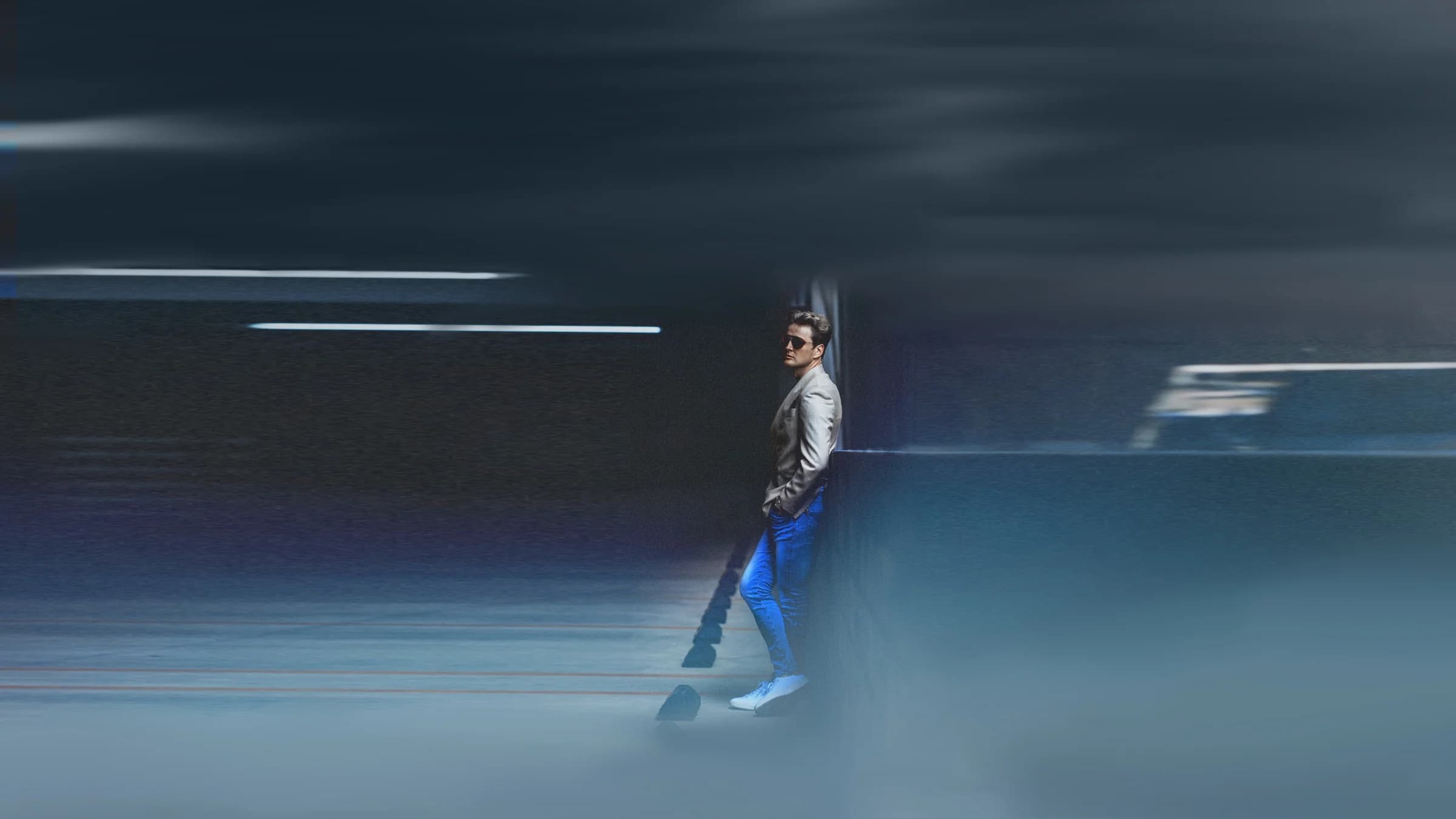A man in a grey blazer standing in a blue-lit hallway