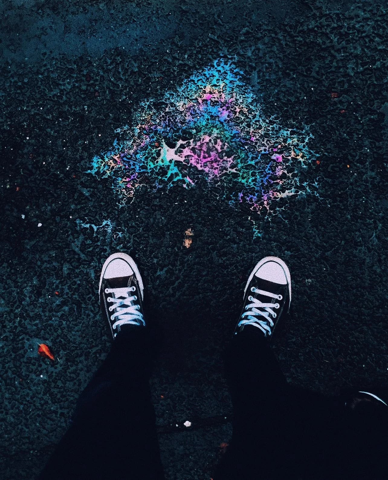 Black sneakers facing a chromatic mark on asphalt