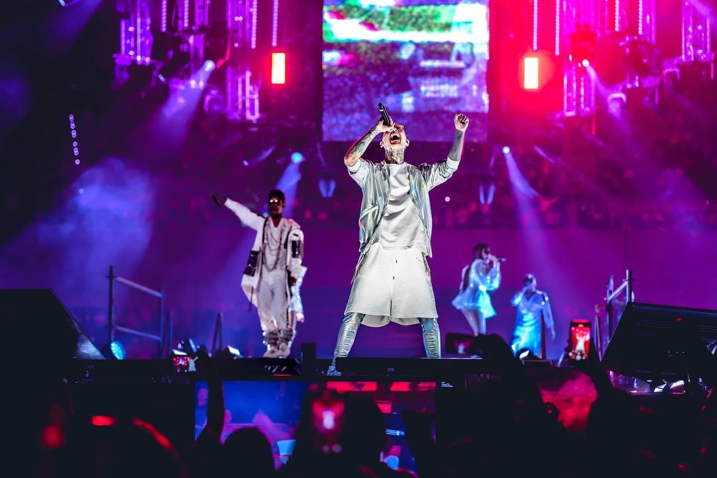 Singer performing on a large concert stage under purple and magenta light