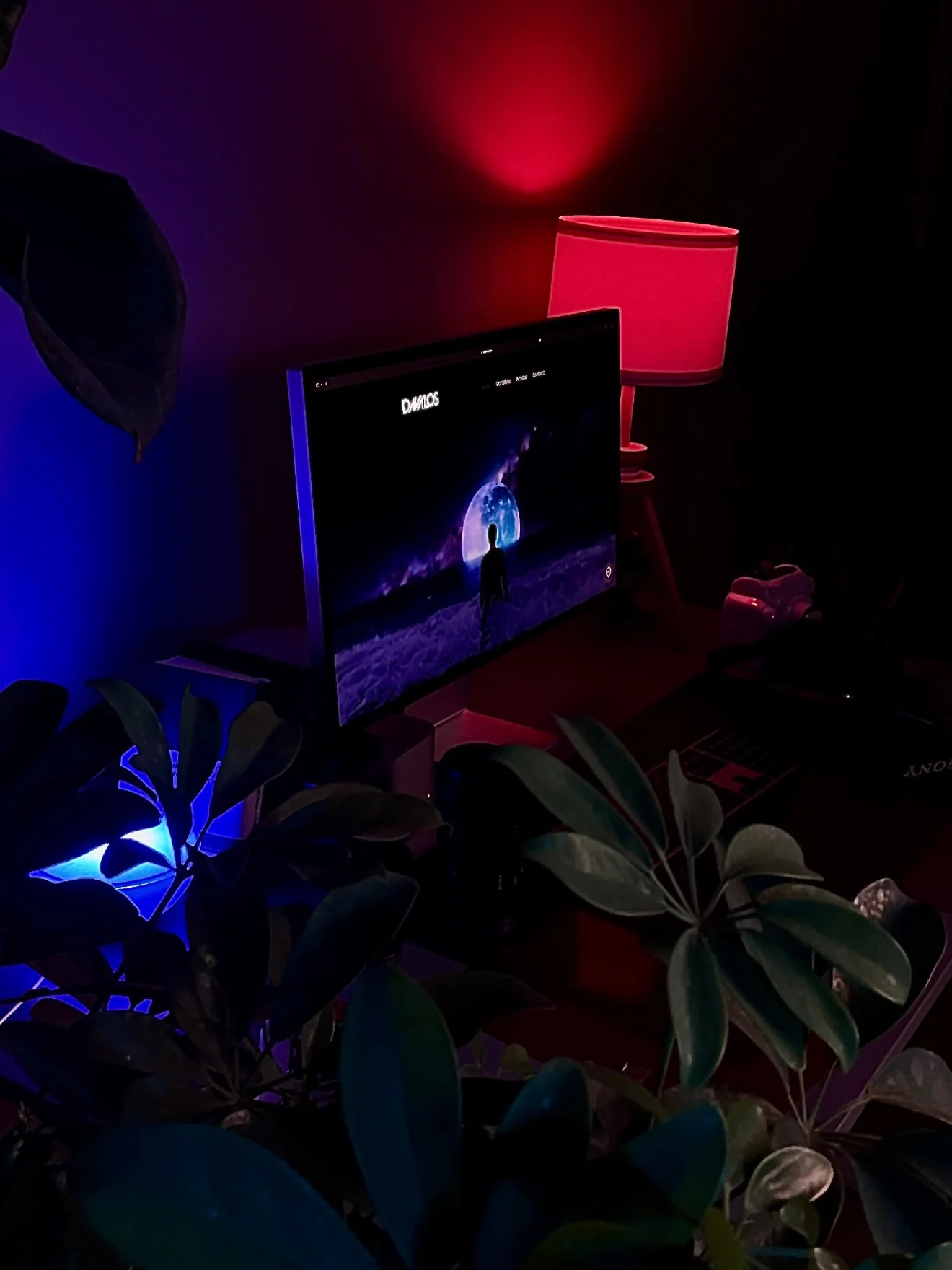 A blue and red lit creative studio with a monitor displaying a moonlit scene