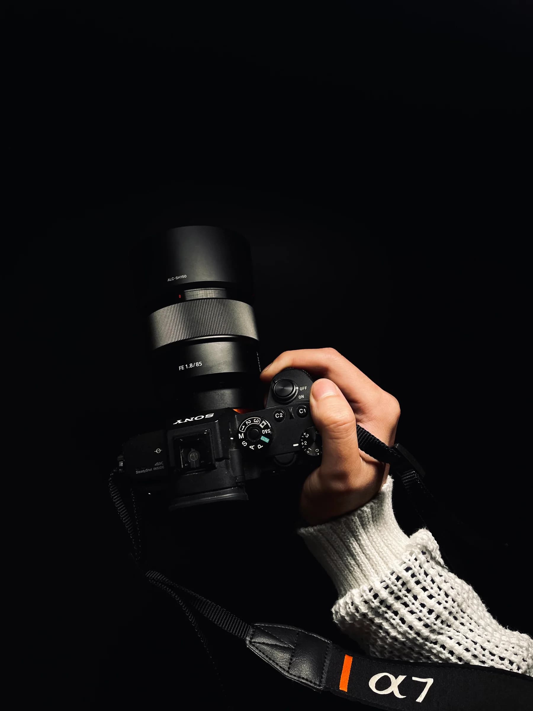 A hand holding a Sony camera against a black background